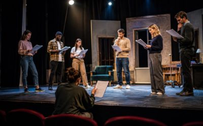 Troupe de théâtre amateur en pleine répétition sur scène sous les projecteurs, guidée par un metteur en scène dans une salle de spectacle