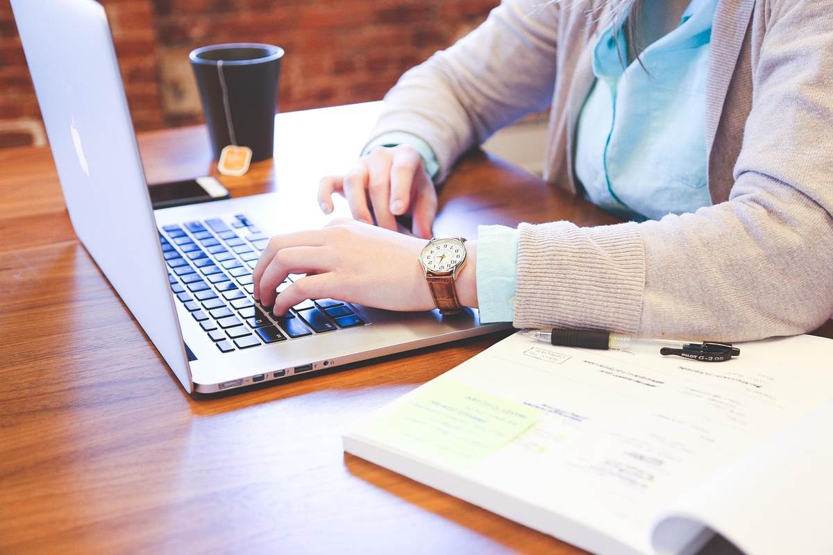 Femme en tenue professionnelle travaillant sur un ordinateur portable à son bureau, avec documents et café à proximité