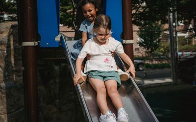 Enfants sur une glissière dans un parc, structures bleues et végétation environnante