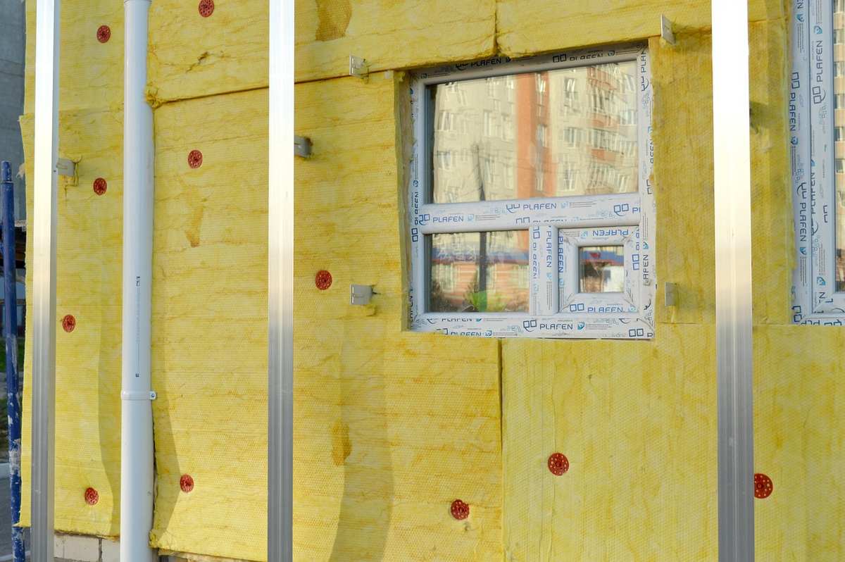 Vue d'une façade isolante avec fenêtre et tuyaux en construction Vue d'une façade isolante avec fenêtre et tuyaux en construction