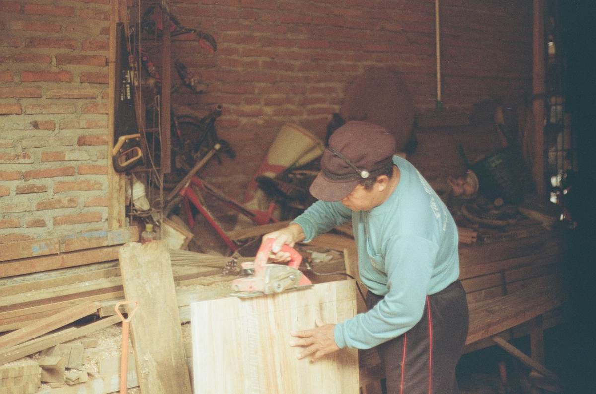 Homme ponçant une planche dans un atelier de menuiserie, outils et bois autour