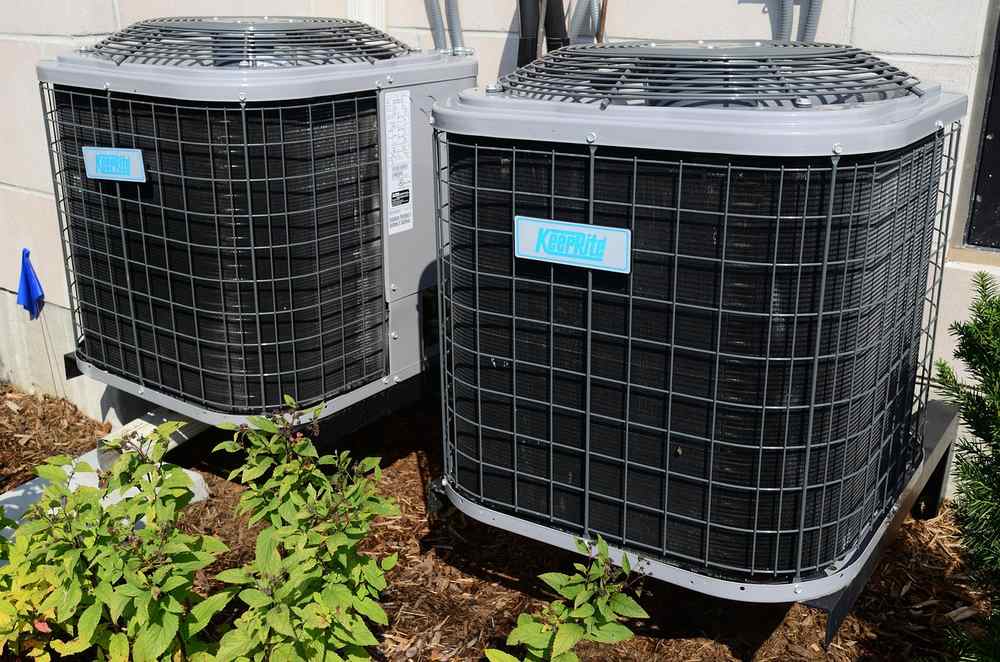 Deux grands climatiseurs extérieurs en acier avec grille, entourés de plantes Deux grands climatiseurs extérieurs en acier avec grille, entourés de plantes